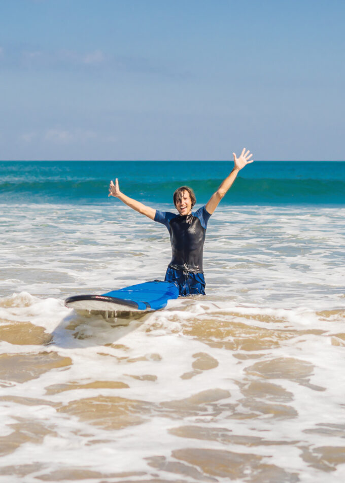 Man carrying surfboard over his head. Close up of handsome guy with surfboard on head at beach. Portrait of man carrying surfboard on hid head and smiling at beach.