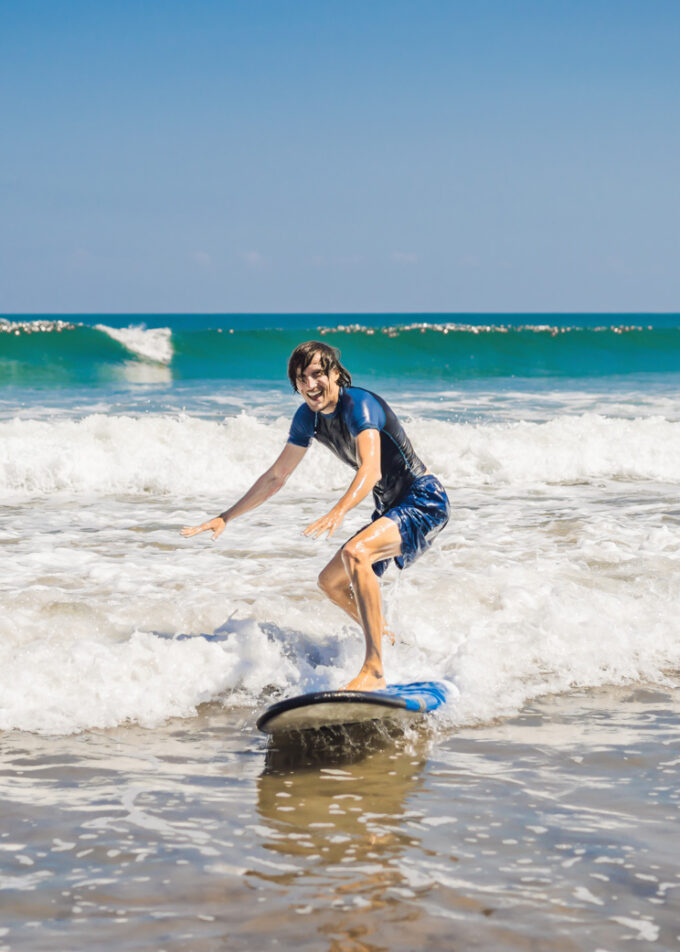 Young man, beginner Surfer learns to surf on a sea foam on the Bali island.