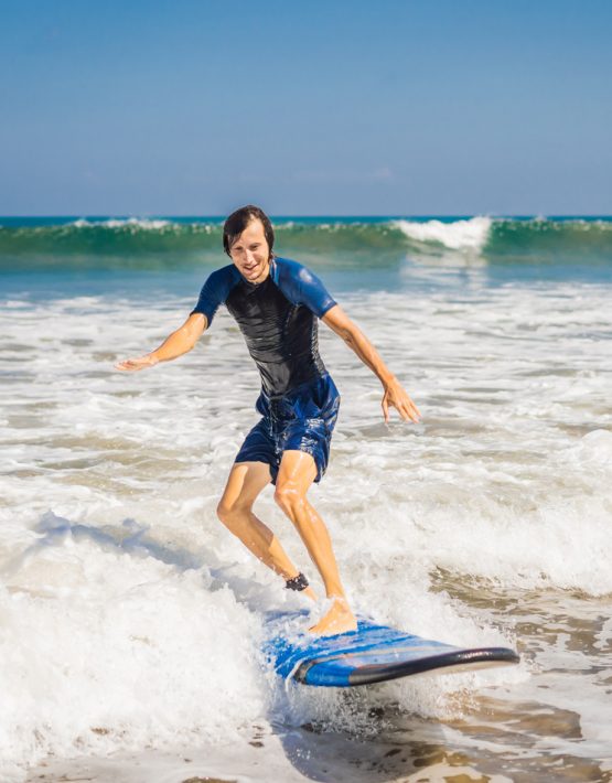 Young man, beginner Surfer learns to surf on a sea foam on the Bali island.