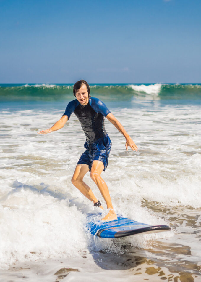 Young man, beginner Surfer learns to surf on a sea foam on the Bali island.